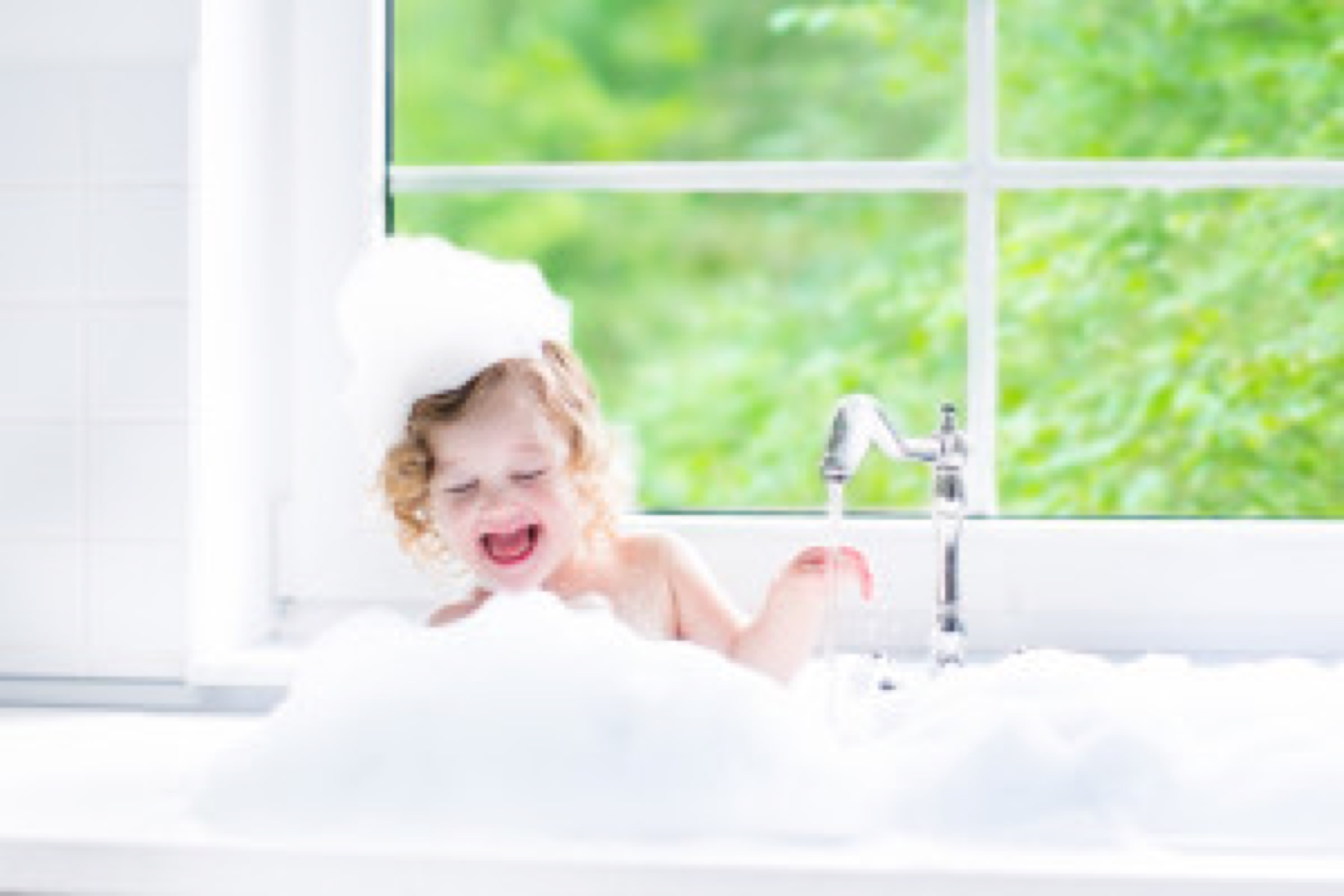 Child taking bath. Little baby in a bath tub washing hair with shampoo and soap. Kids playing with foam and water splashes. White bathroom with window. Clean kid after shower. Children hygiene.