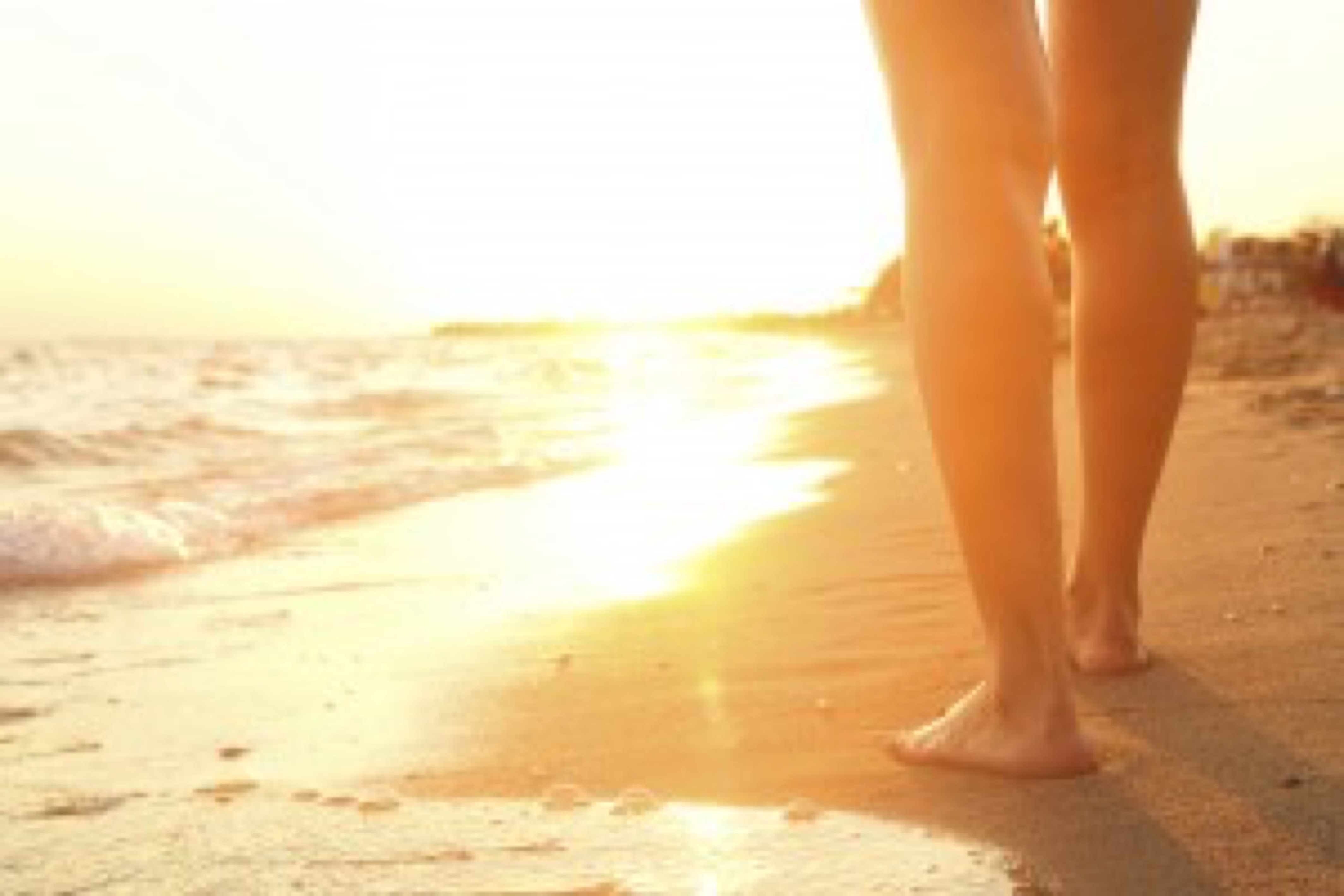 A young woman walking on the sand. A beautiful sunset in her front.